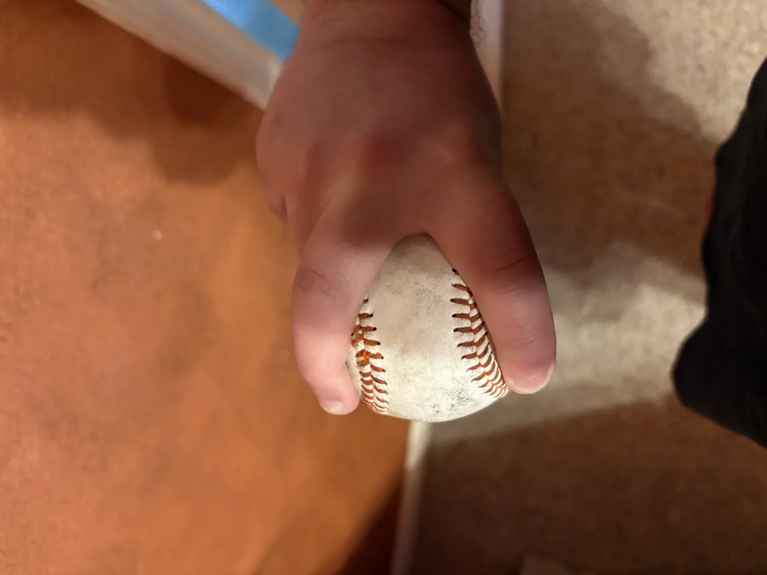 A hand gripping a baseball splitter style, index and middle fingers spread wide just outside the seams.