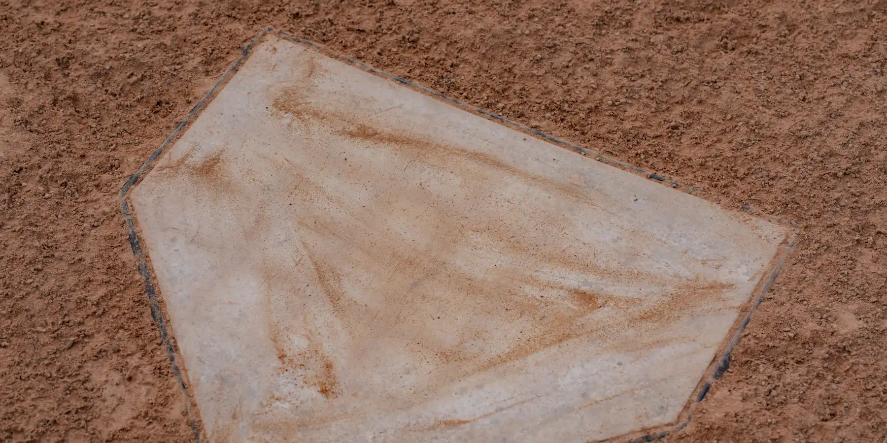 A worn white home plate set into reddish infield dirt, marked by game use.