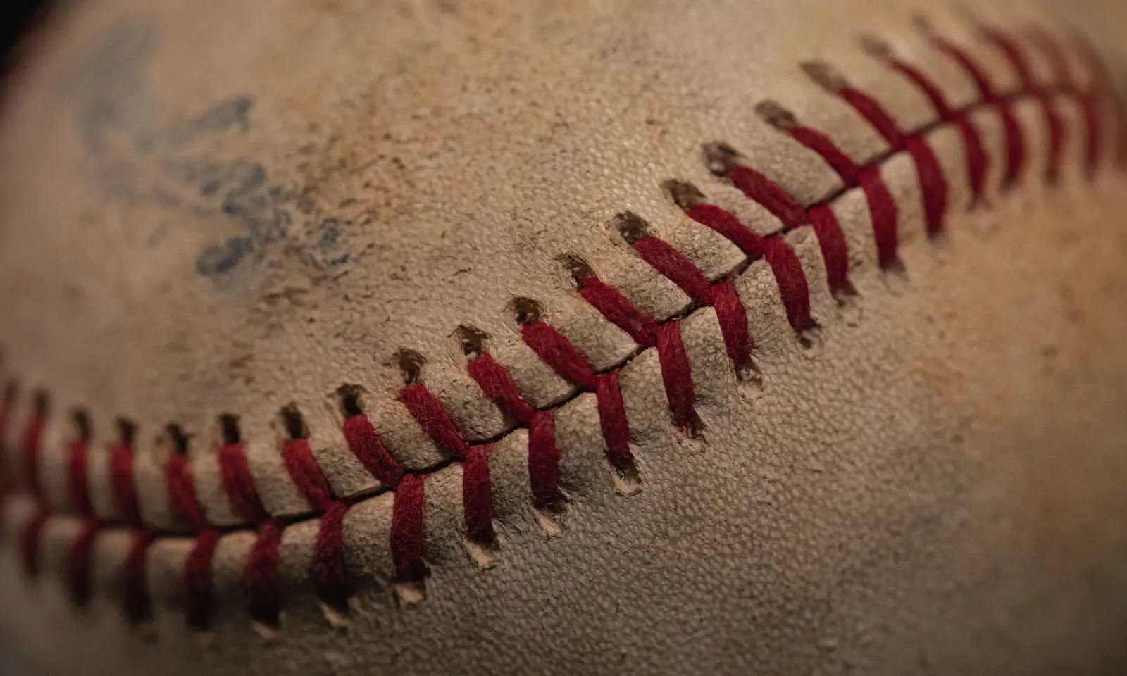 A close crop of a game-used baseball with scuffed leather and raised red stitching.